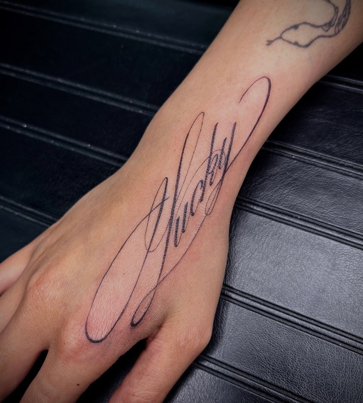 Cursive word tattoo in black ink on the back of a person's hand.