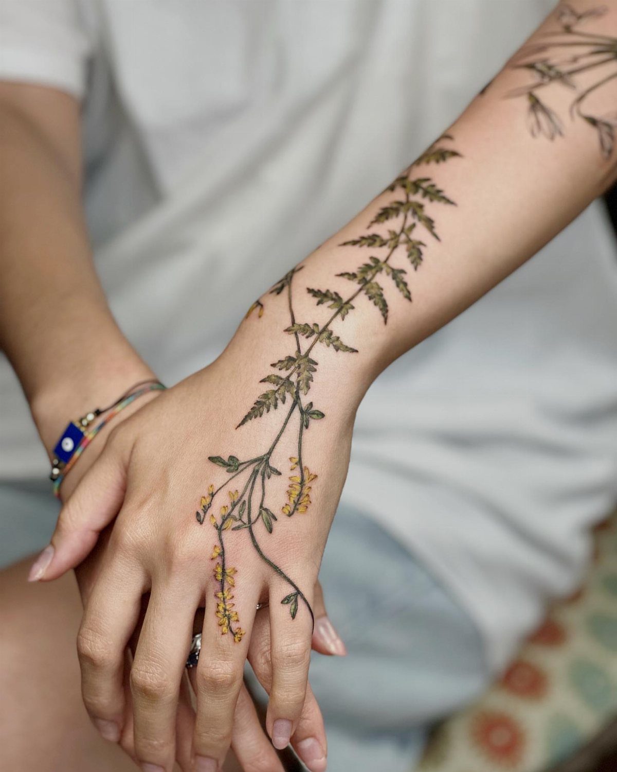 Botanical branch tattoo with yellow flowers on a person's hand and forearm.