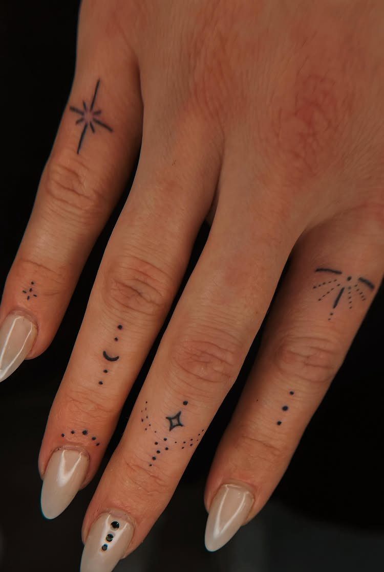 Hand with minimalist finger tattoos including a star, moon, and small dotted patterns.