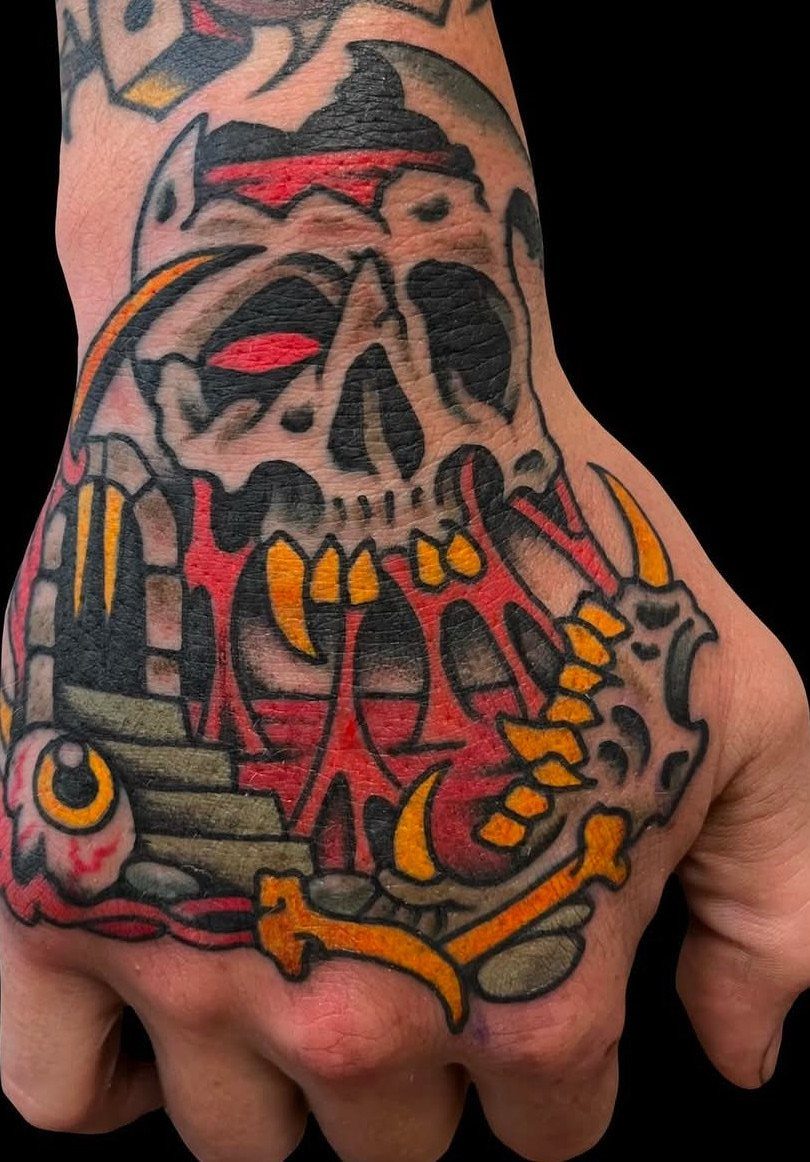 Traditional skull tattoo with red and yellow details covering the back of a hand.