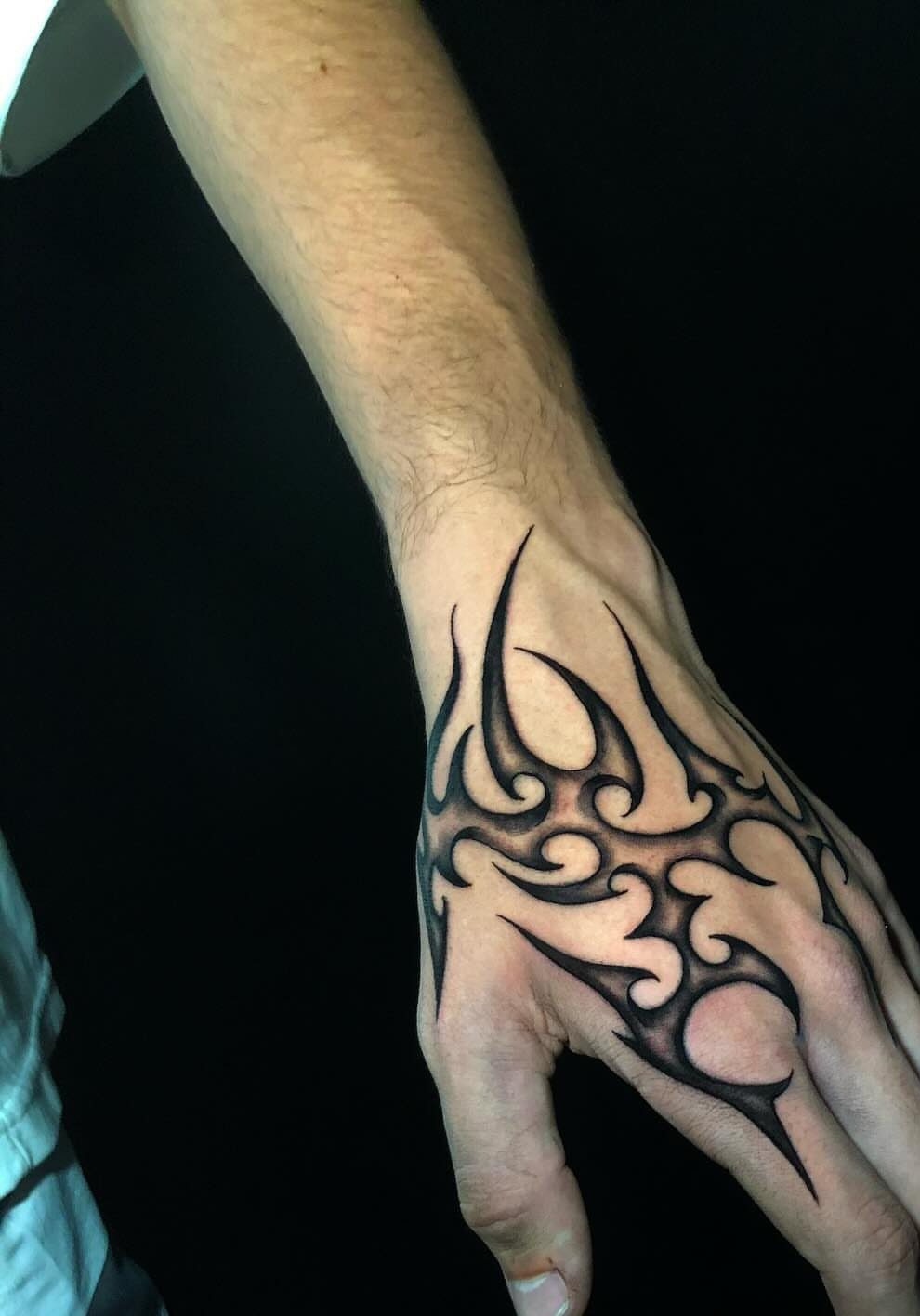 Tribal tattoo with bold black curving lines on the back of a hand.