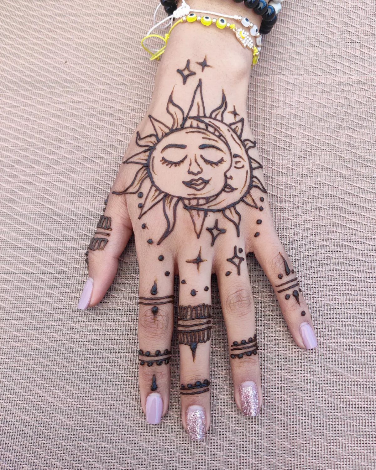 6 Hand Tattoo Henna Style Ideas for Every Taste 6 Hand with brown henna tattoo of a sun and crescent moon face and stars.