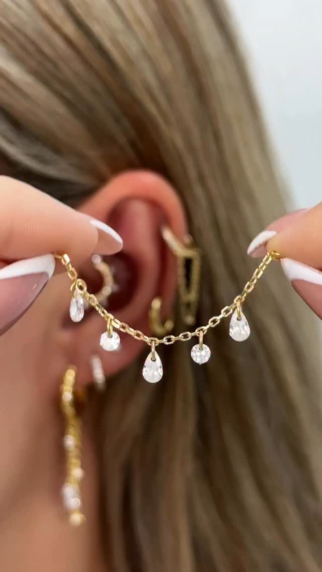 Hanging Ear Piercing Ideas: 6 Chain, Pearl and Star Styles 1 Gold chain with teardrop gemstones connecting two ear piercings on a person.