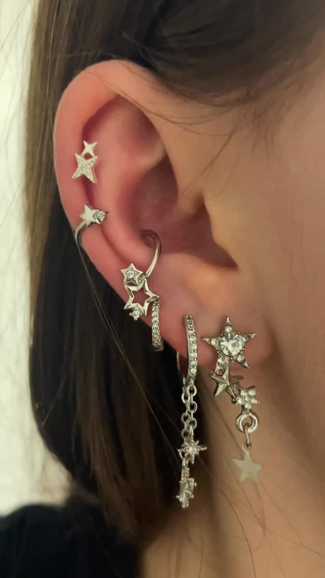 Hanging Ear Piercing Ideas: 6 Chain, Pearl and Star Styles 6 Ear with multiple silver piercings featuring hanging star charms and sparkling star studs.