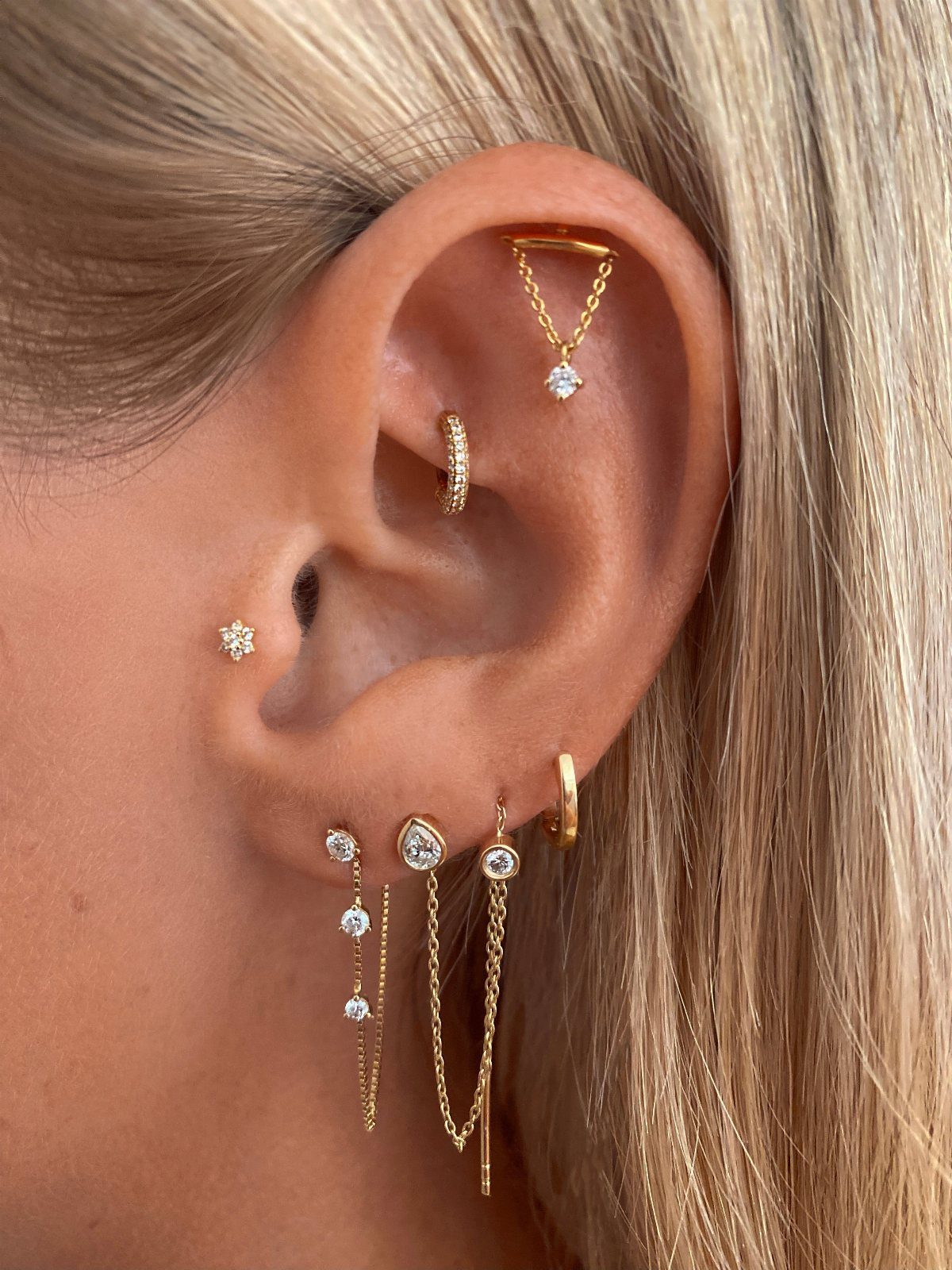 Hanging Ear Piercing Ideas: 6 Chain, Pearl and Star Styles 4 Ear with multiple gold piercings and minimalist hanging gold chain earrings with gemstones.