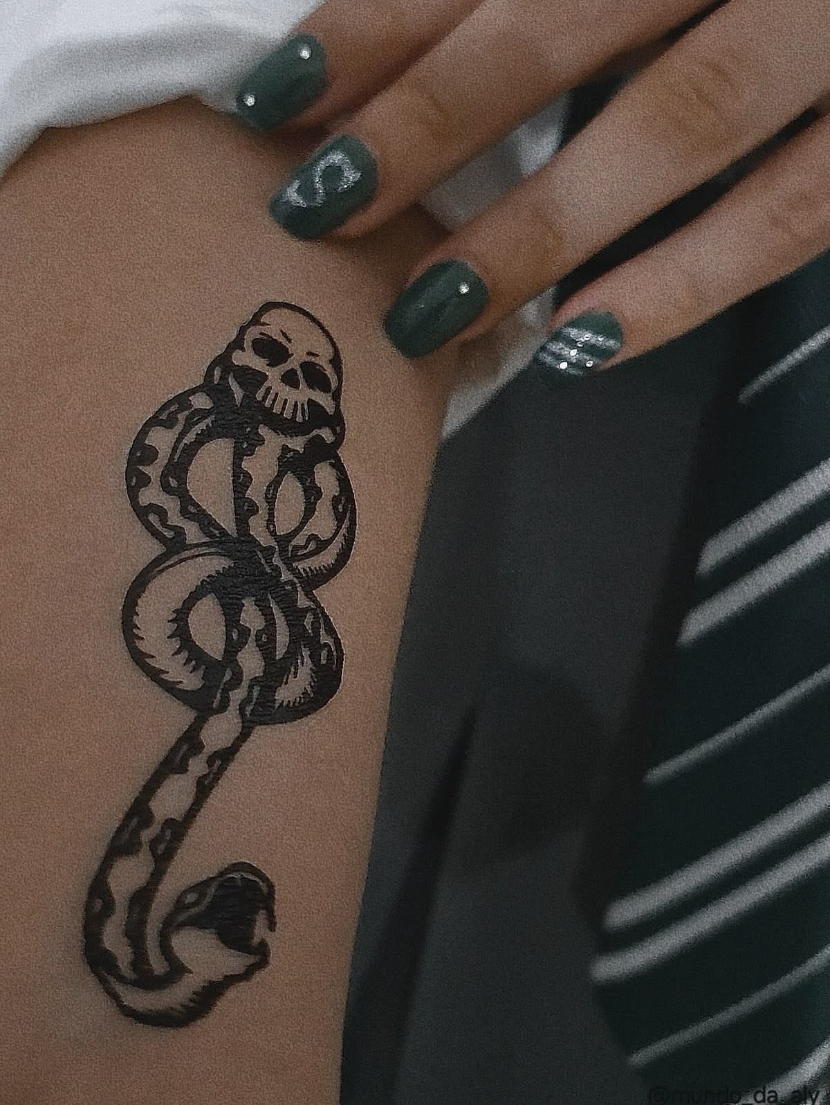 Skull and snake tattoo on an arm with dark green nail polish