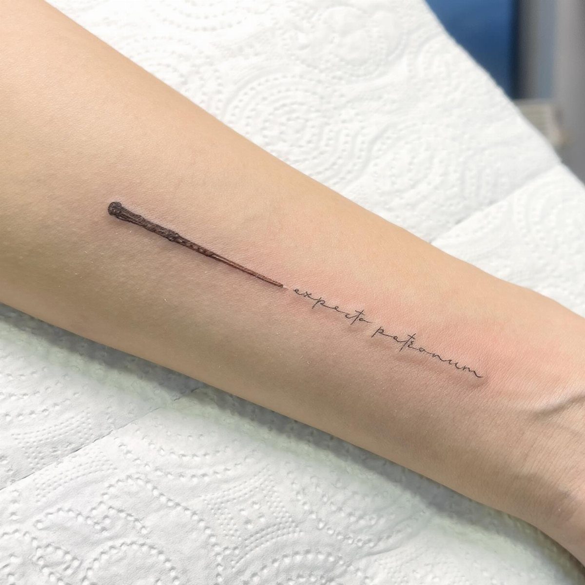 Magic wand and Expecto Patronum script tattoo on a person's forearm.