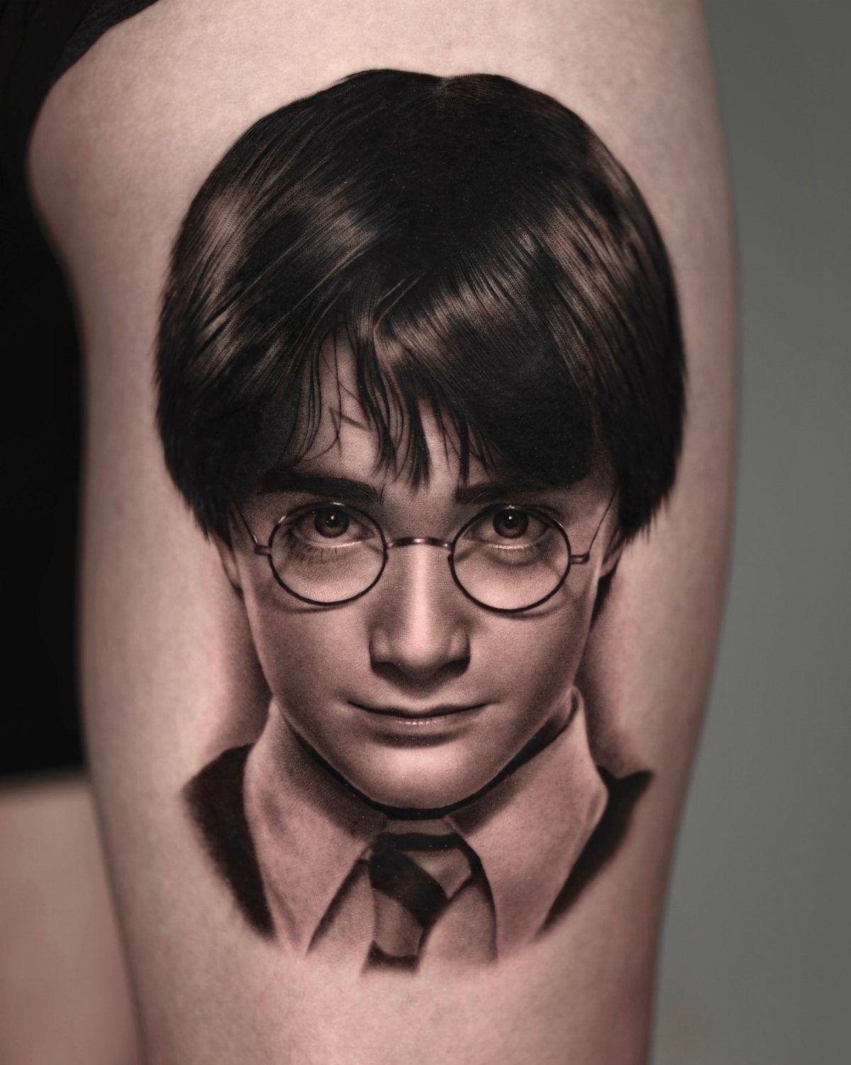 Harry Potter portrait tattoo in black and grey ink on a person's arm.