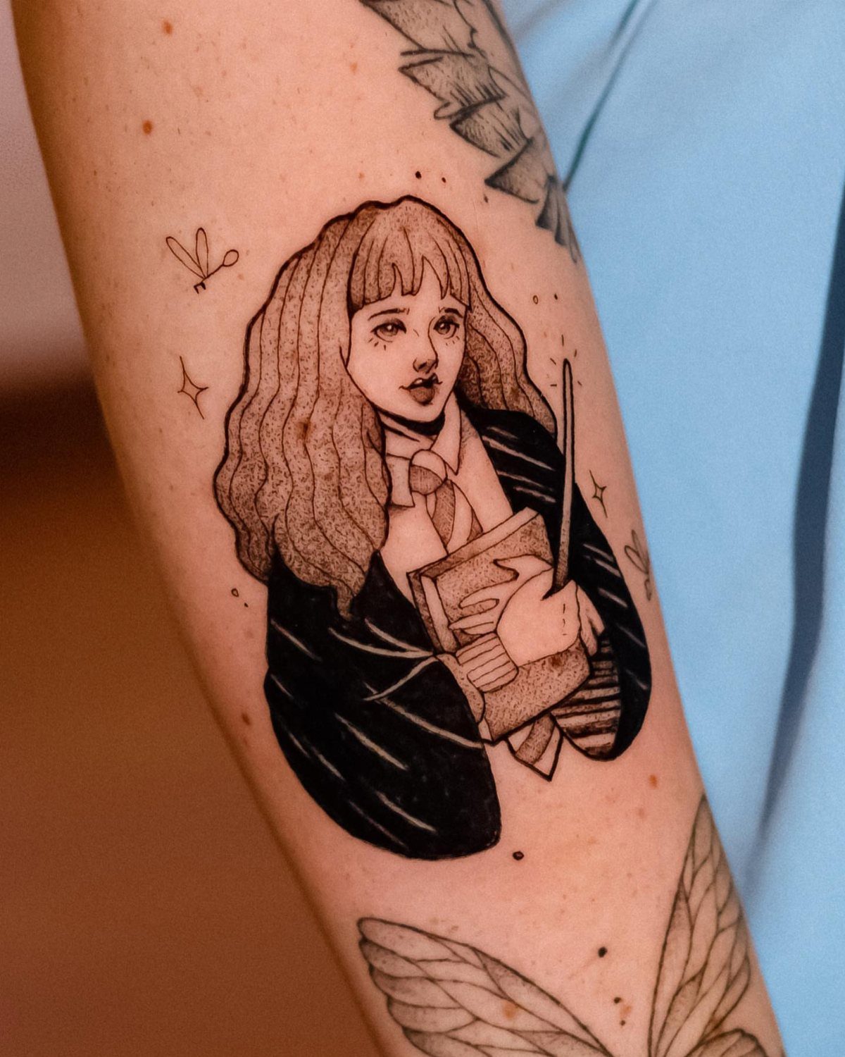 Tattoo of Hermione Granger holding a book and wand on a person's arm.