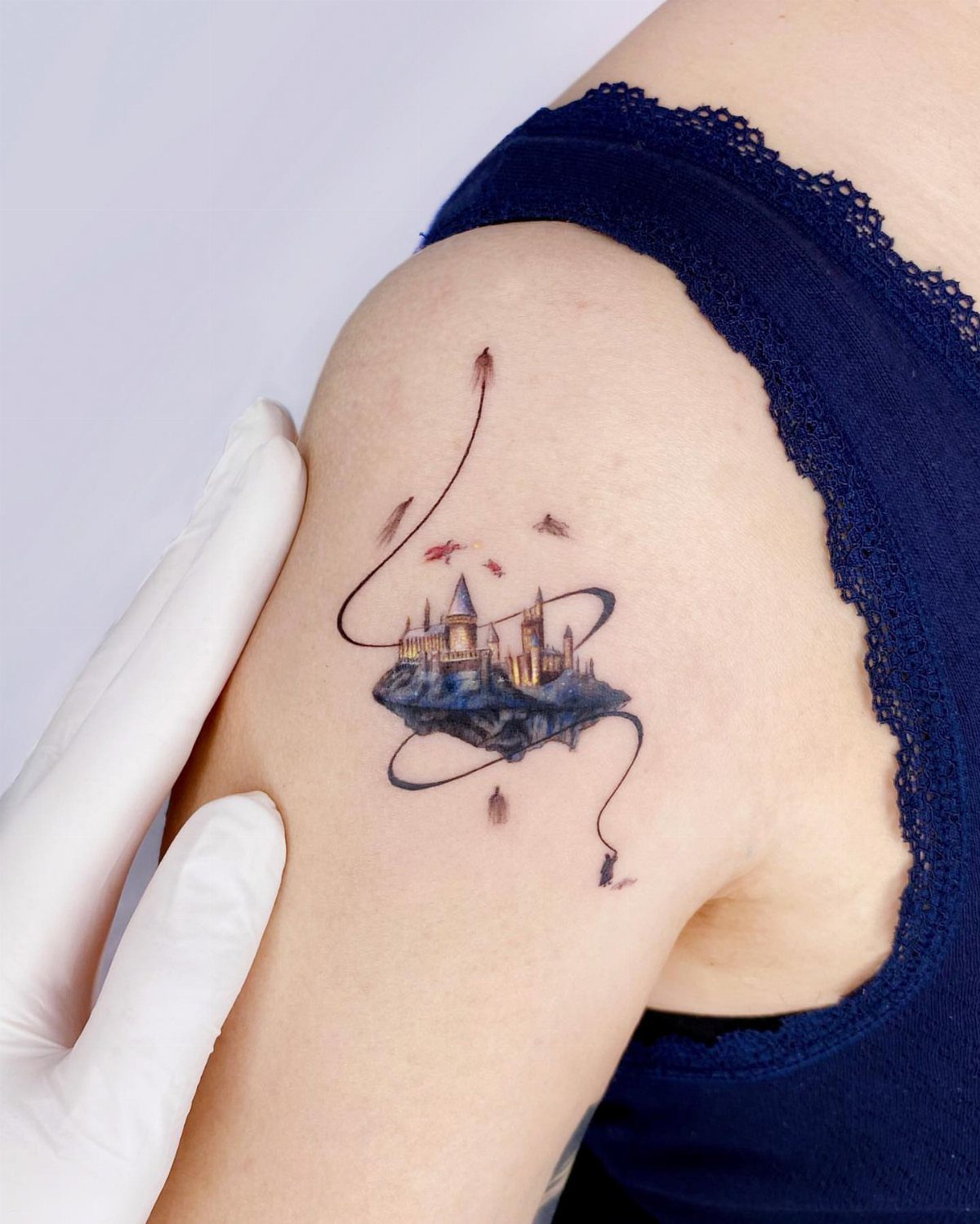 Hogwarts castle tattoo on an upper arm with swirling black ink lines.