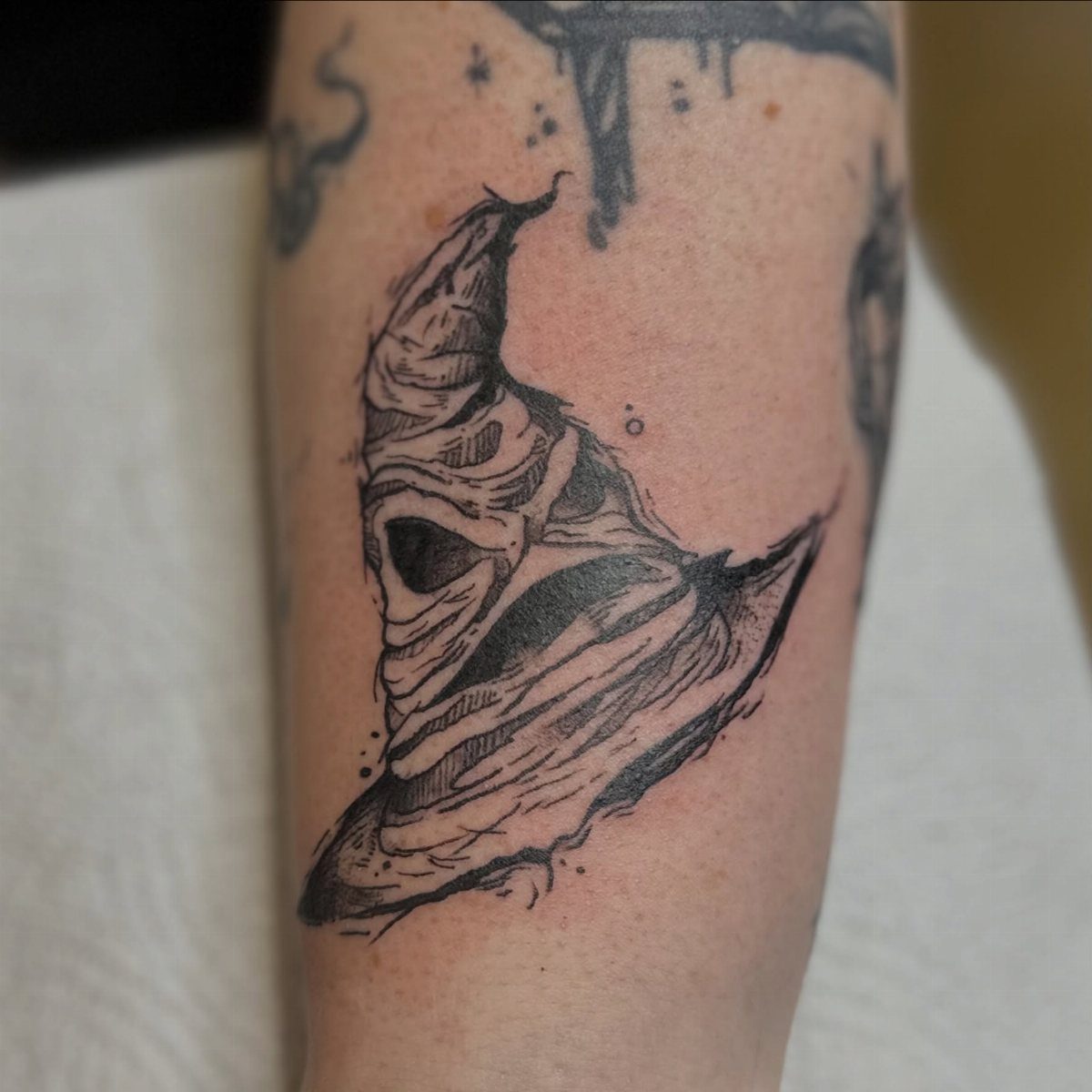 Sorting Hat tattoo in black ink on a person's arm with detailed folds