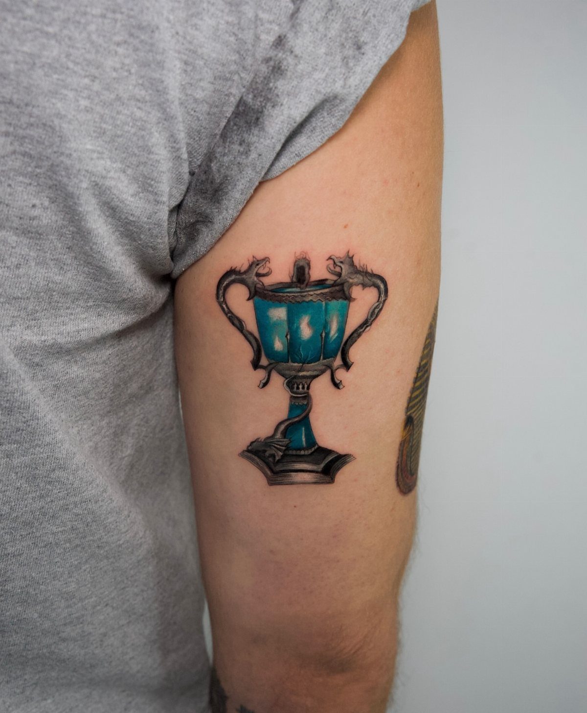 Triwizard Cup tattoo with glowing blue center on a person's upper arm
