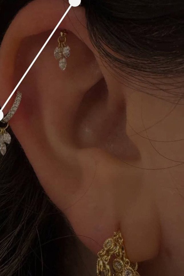Ear with gold crystal helix piercing and a gold hoop earring.