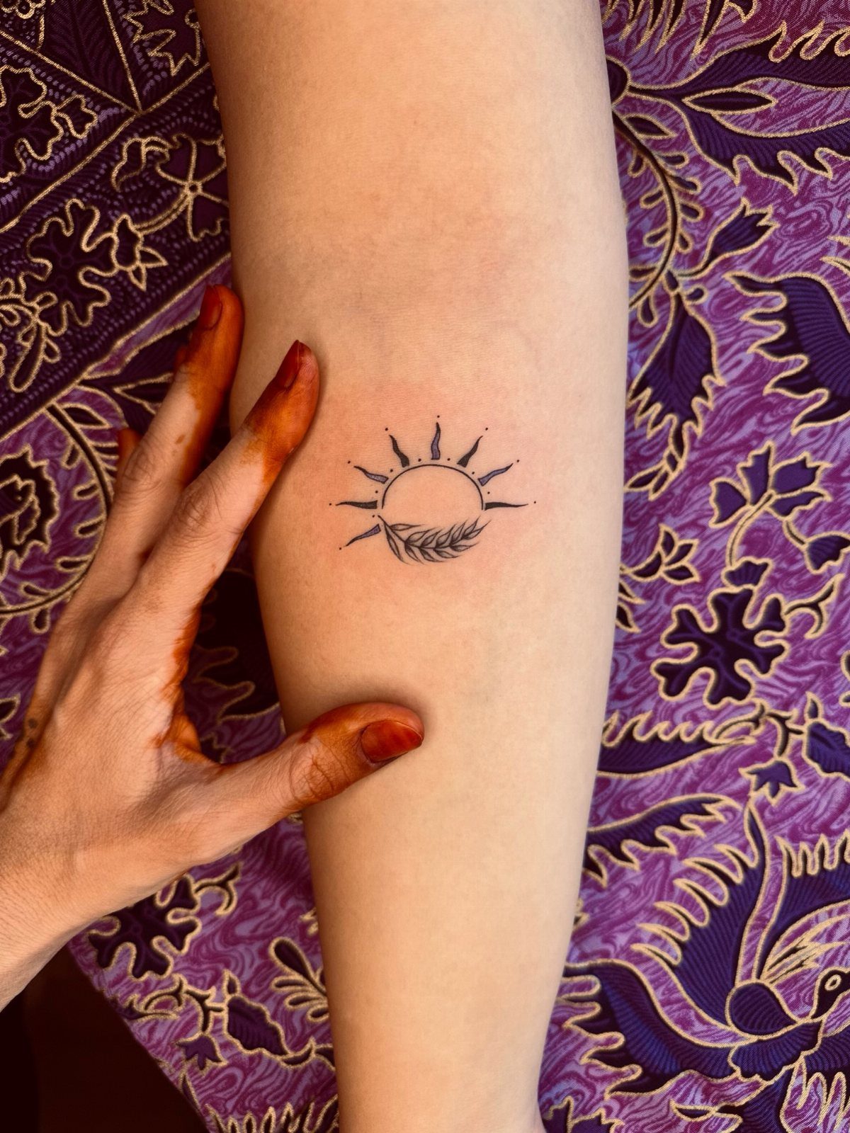 Sun tattoo with rays and leaves on a forearm with a hand pointing.