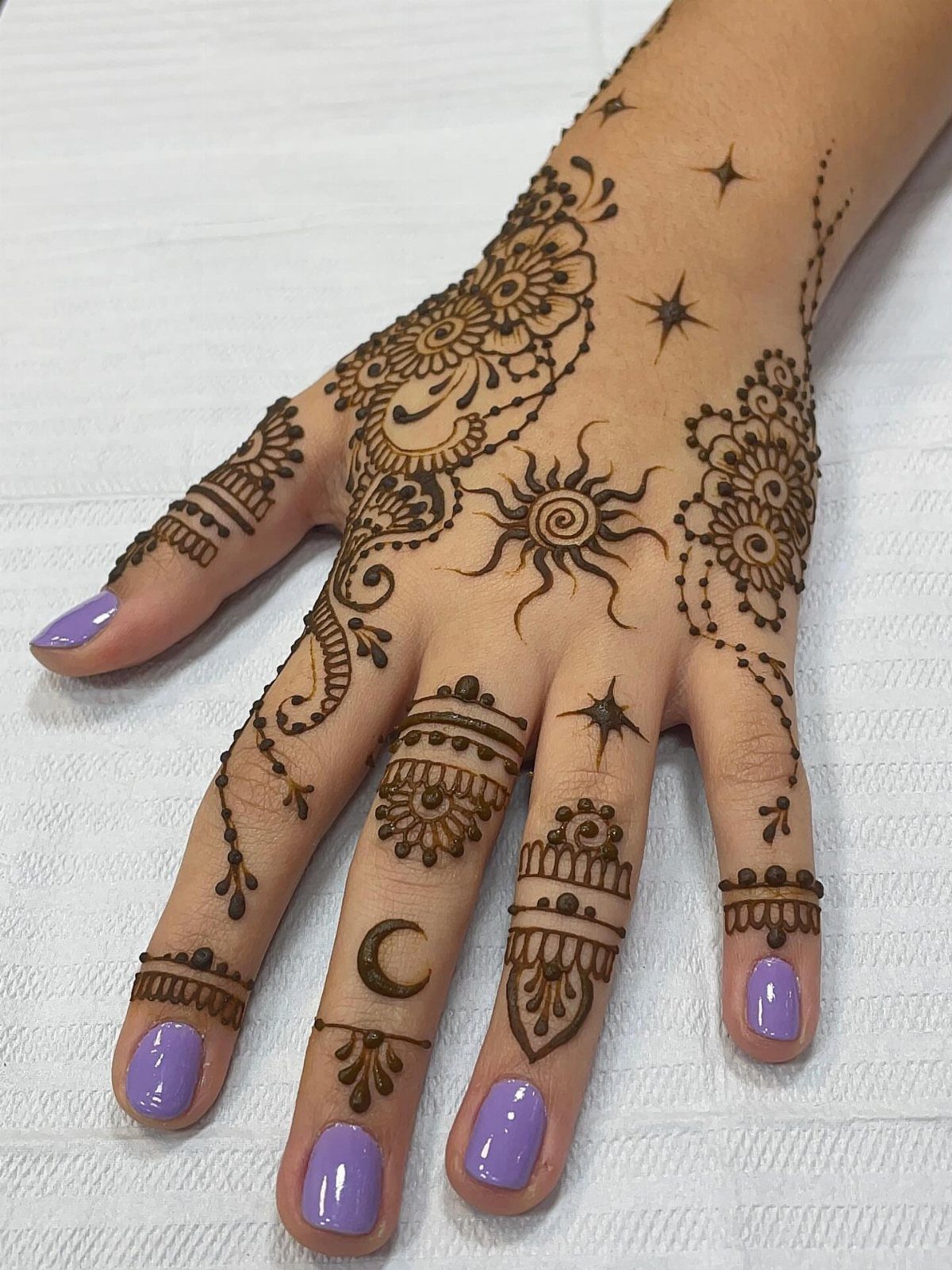 Henna sun tattoo on the back of a hand with purple nail polish.