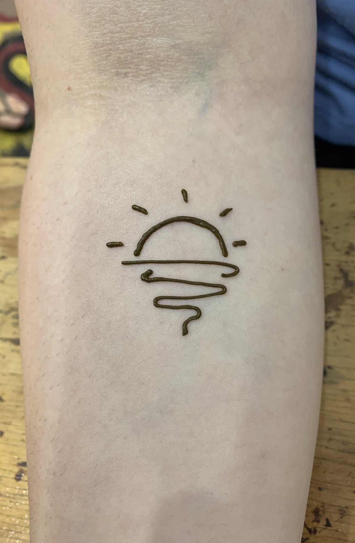 Simple henna sun tattoo with wavy lines on a person's pale skin
