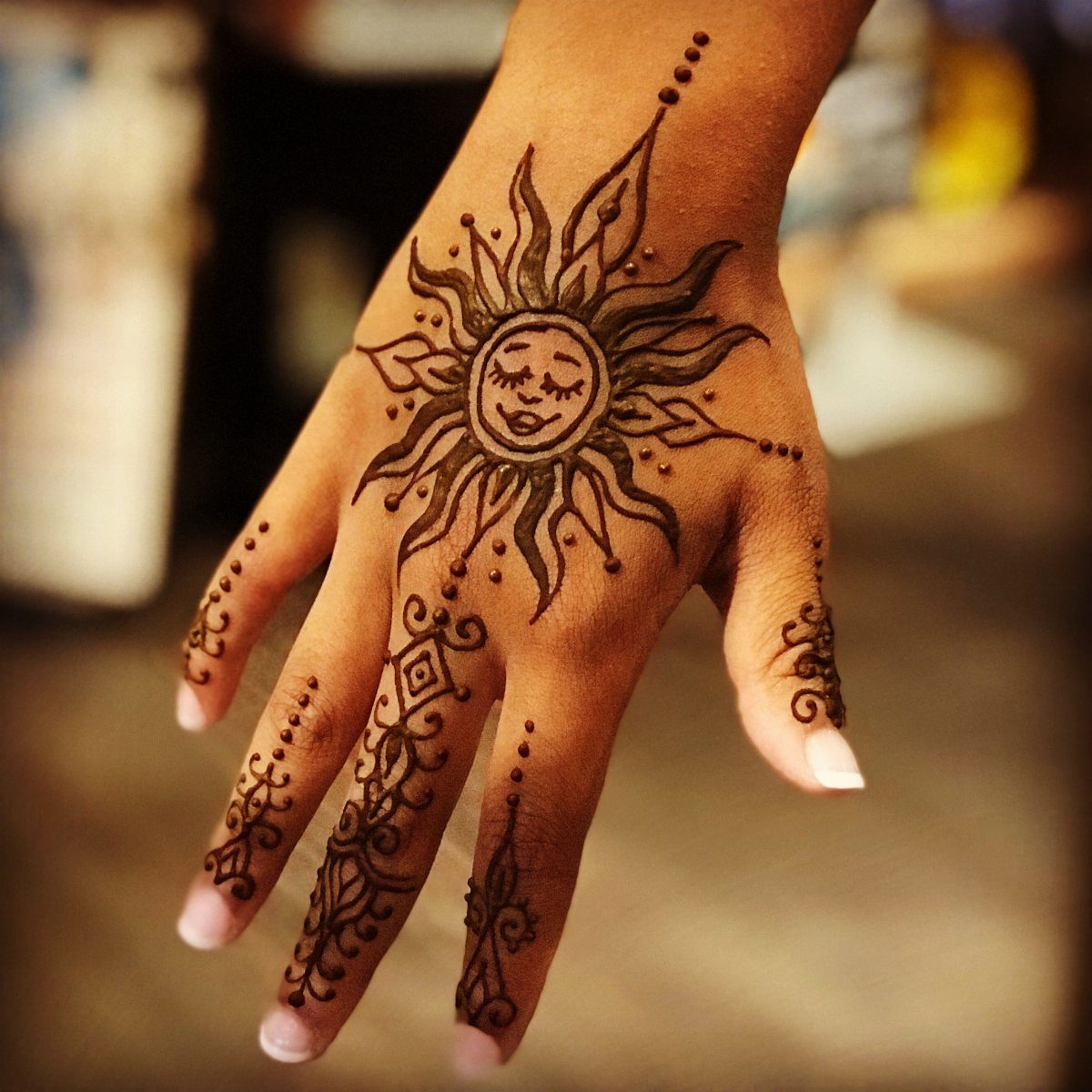 Henna tattoo of a smiling sun with radiating rays on a person's hand.