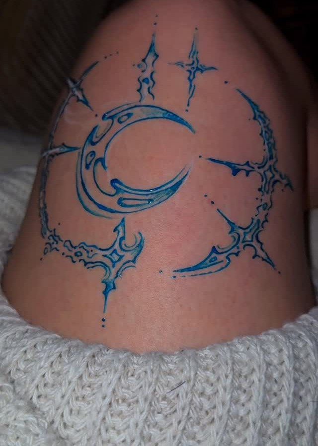 Blue henna tattoo of a crescent moon with jagged rays on a shoulder