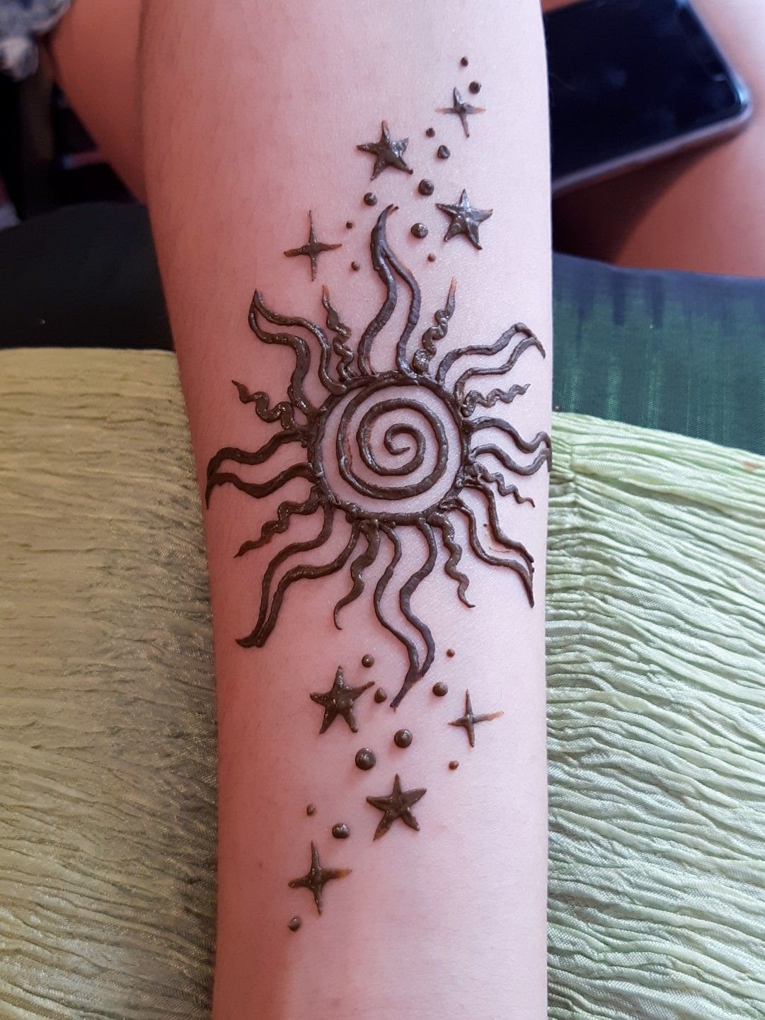 Henna sun tattoo with a spiral center and stars on a forearm