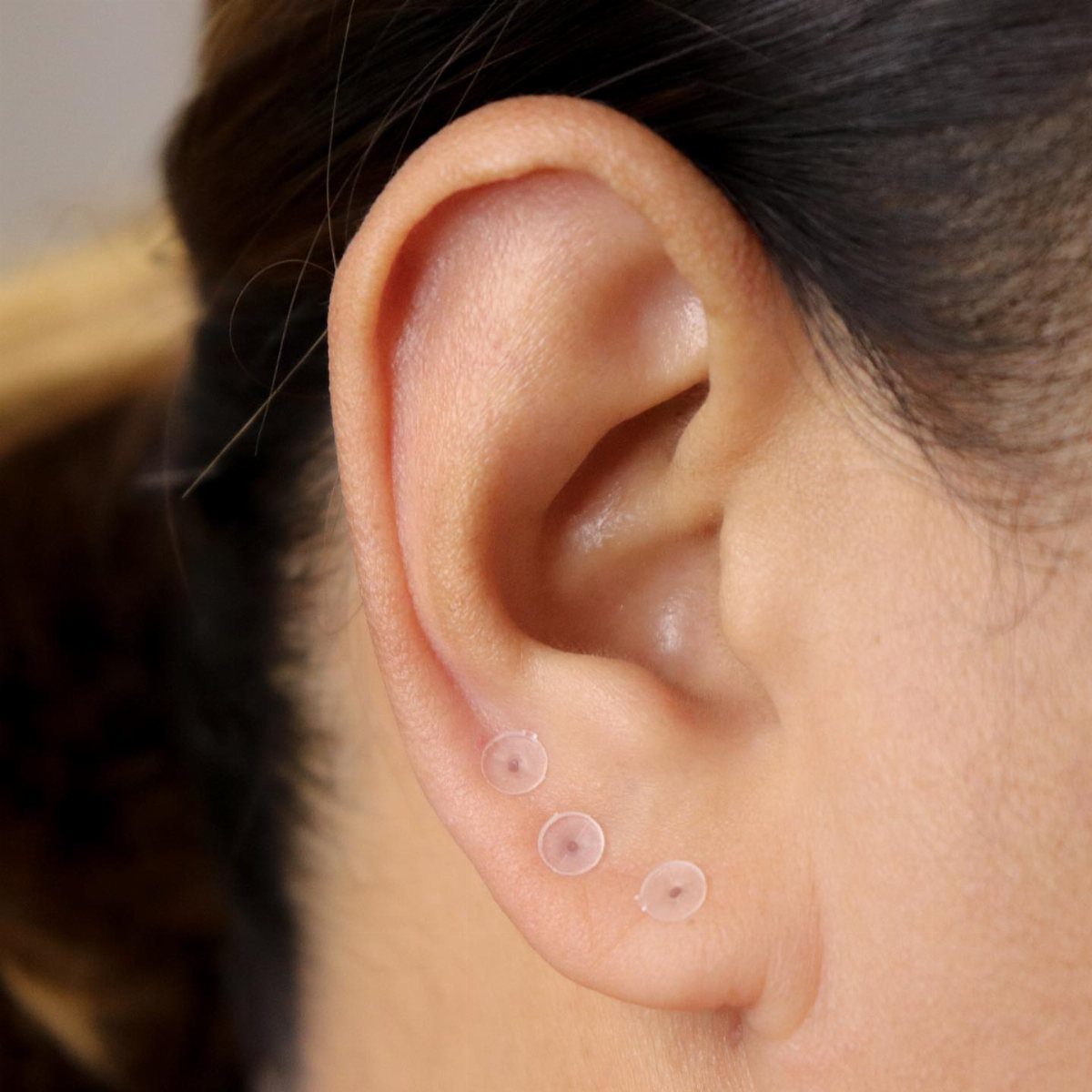 Ear lobe with three translucent clear retainers in the piercing holes
