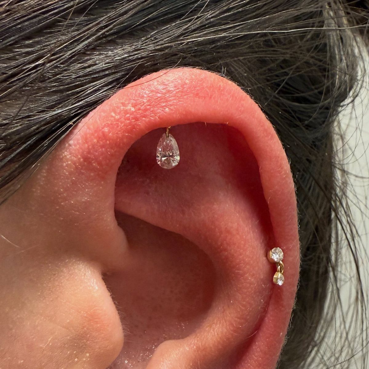 Human ear featuring a floating teardrop gemstone helix piercing and a gold stud.