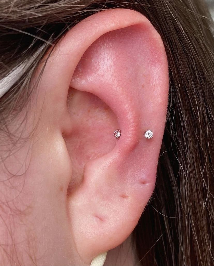 Human ear with two small clear gemstone studs, one placed in a hidden position.
