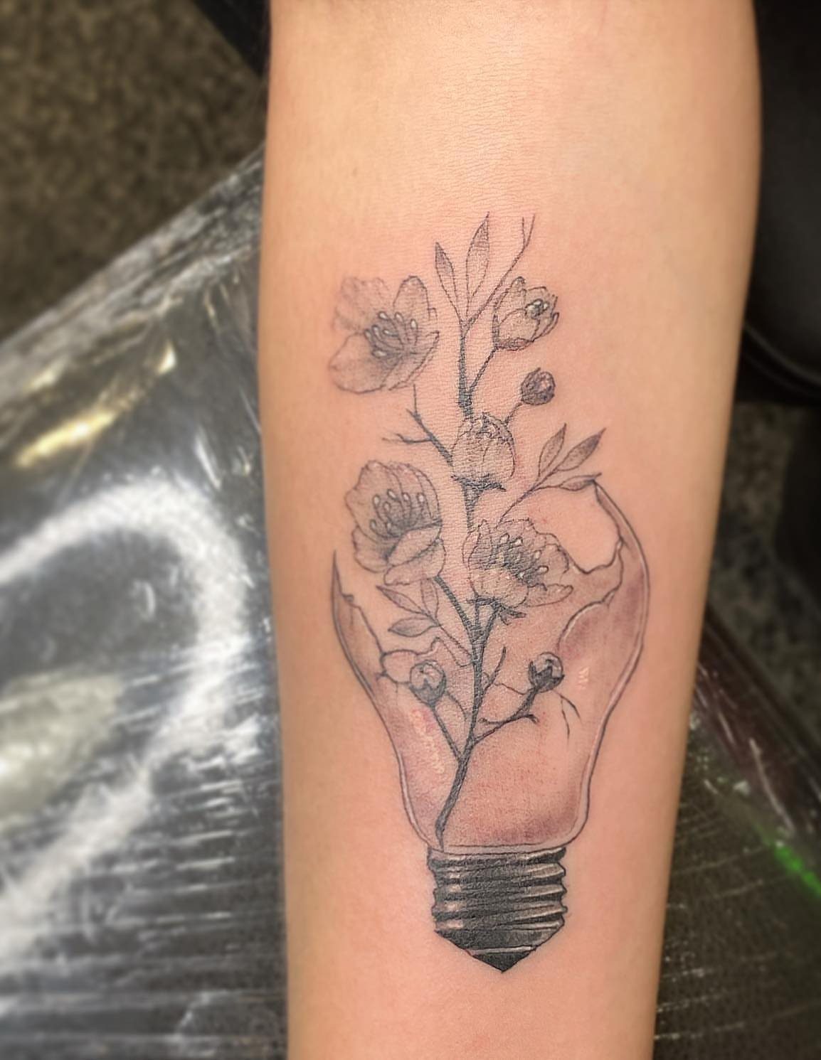 Lightbulb tattoo with flowers growing inside and out of the top on skin