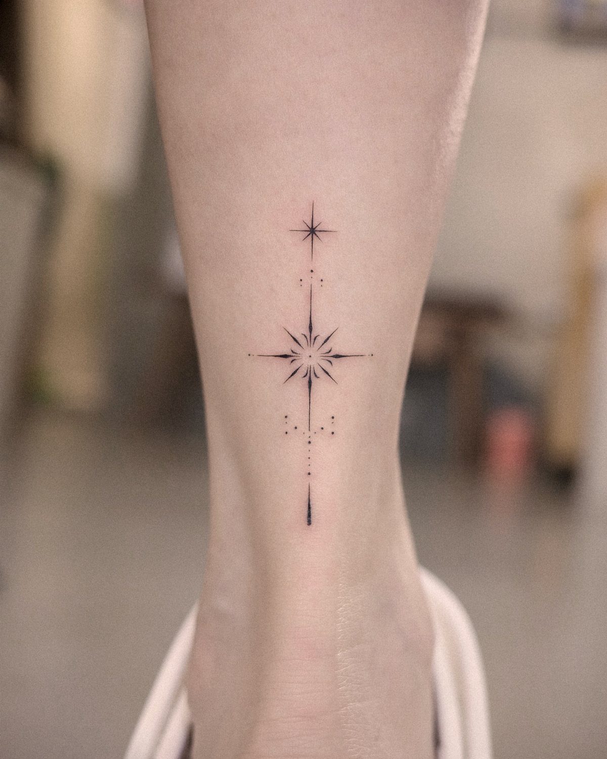 Four-pointed star tattoo with dots aligned vertically on a person's ankle.