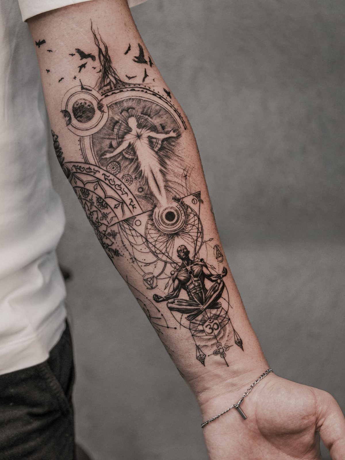 Seated meditative figure tattoo with sunburst and geometric patterns on a forearm