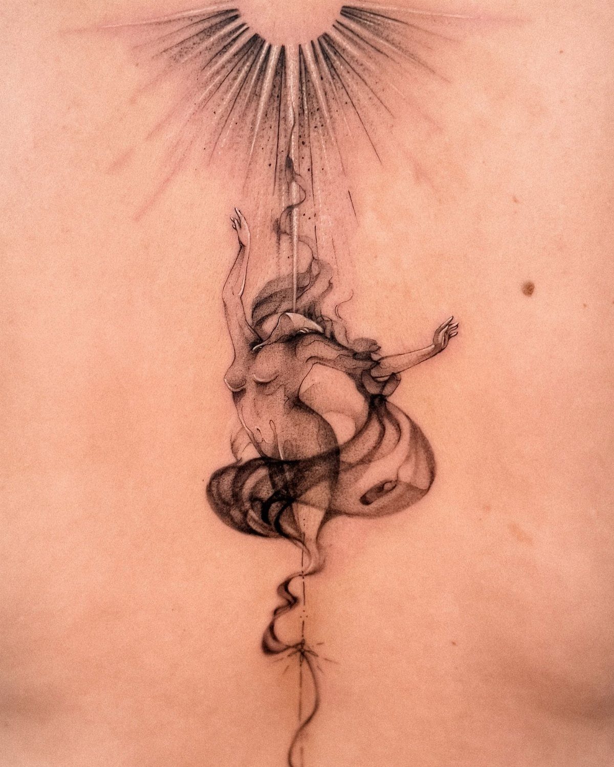 Tattoo of a woman reaching toward a radiant sunburst on a person's back.