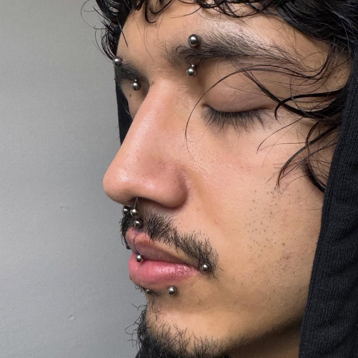 Person with silver piercings in their eyebrows, nose, and lips in a close-up profile.