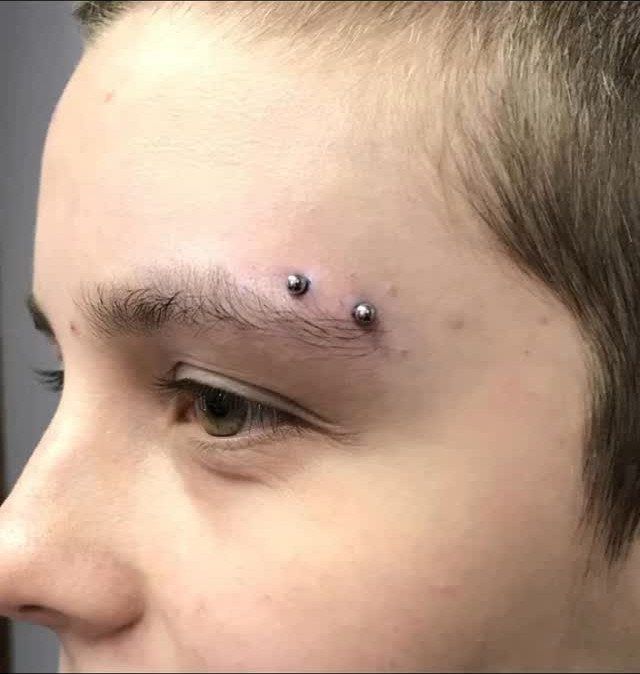 Horizontal eyebrow piercing with silver metal beads on a person's face