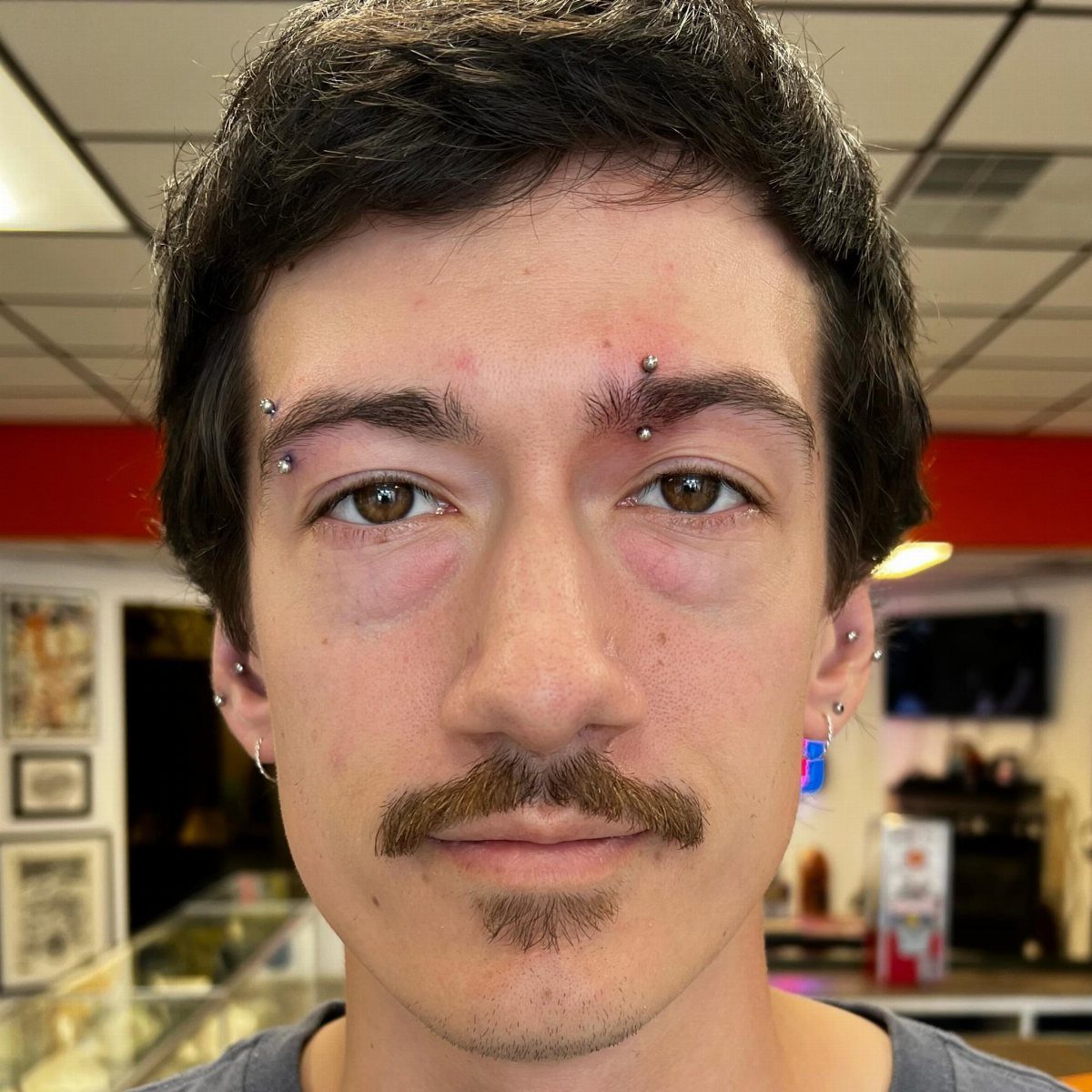 Man with multiple curved barbell piercings in his eyebrows and earlobes.