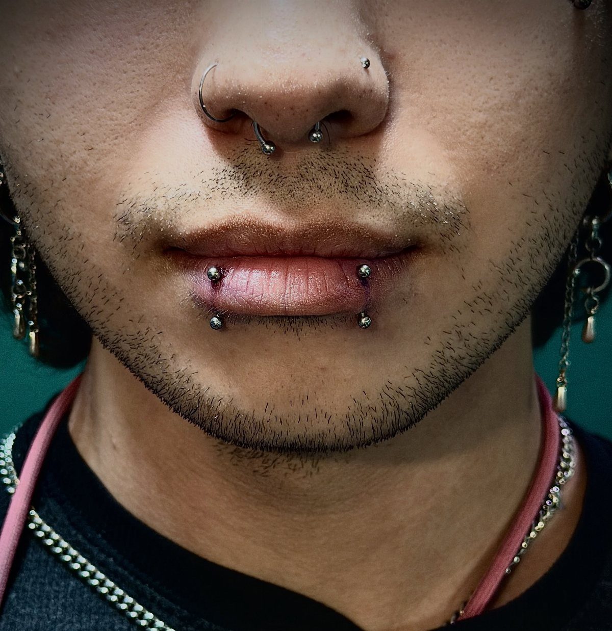 Person with multiple facial piercings including a septum ring and lip studs