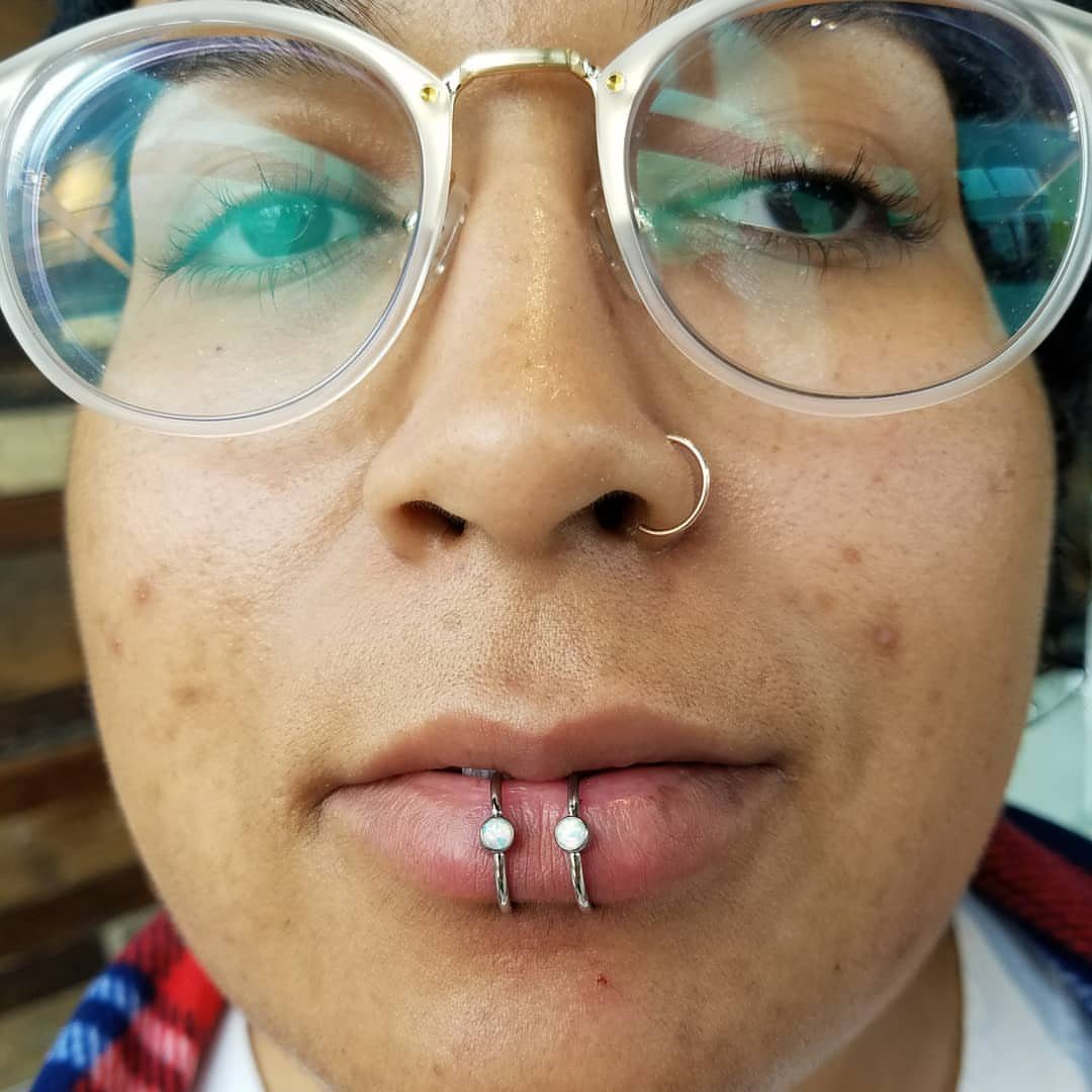 Person with round glasses, a nose ring, and two beaded lip piercings.