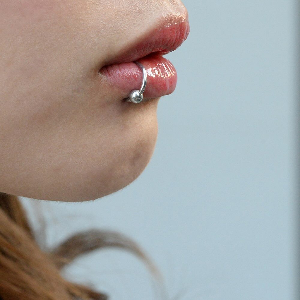 Silver captive bead ring piercing on a person's lower lip.