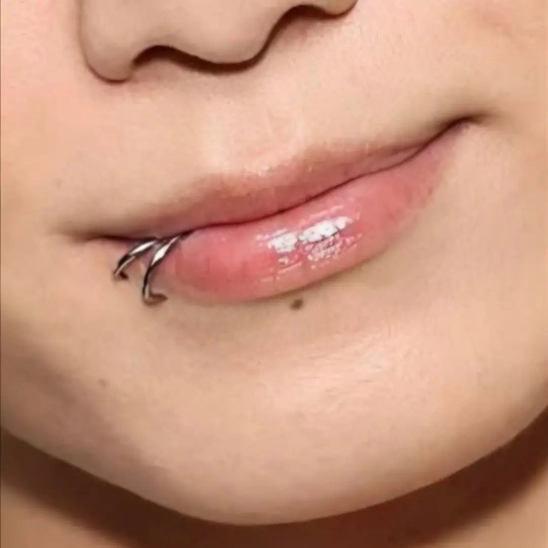 Lower lip with glossy pink lipstick and two silver hoop piercings on the side.