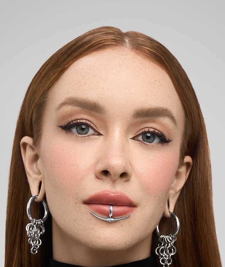 Woman with red hair wearing a silver horseshoe lip piercing and chain hoop earrings.