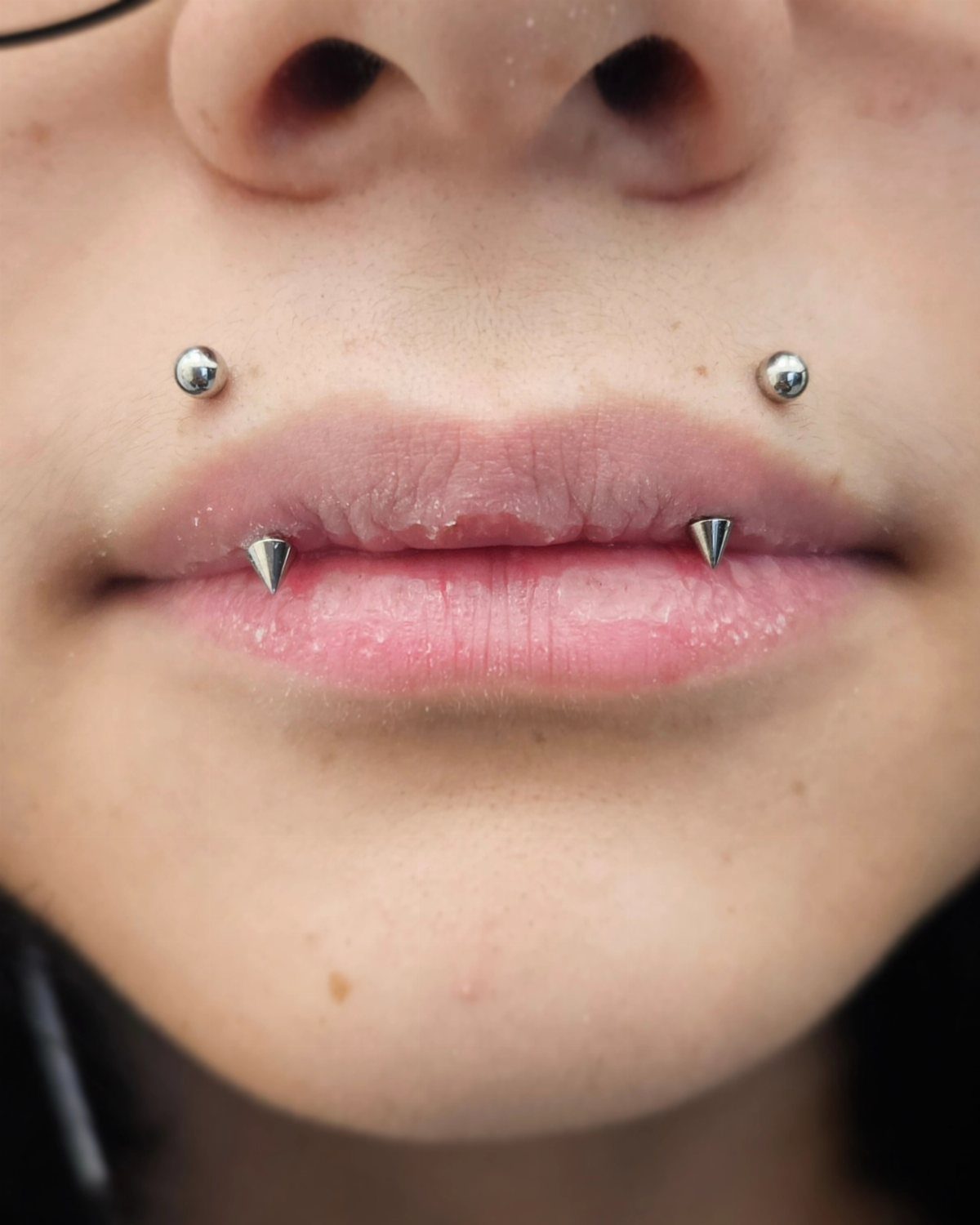 Silver lip piercings including two conical spikes on the lower lip and two balls.