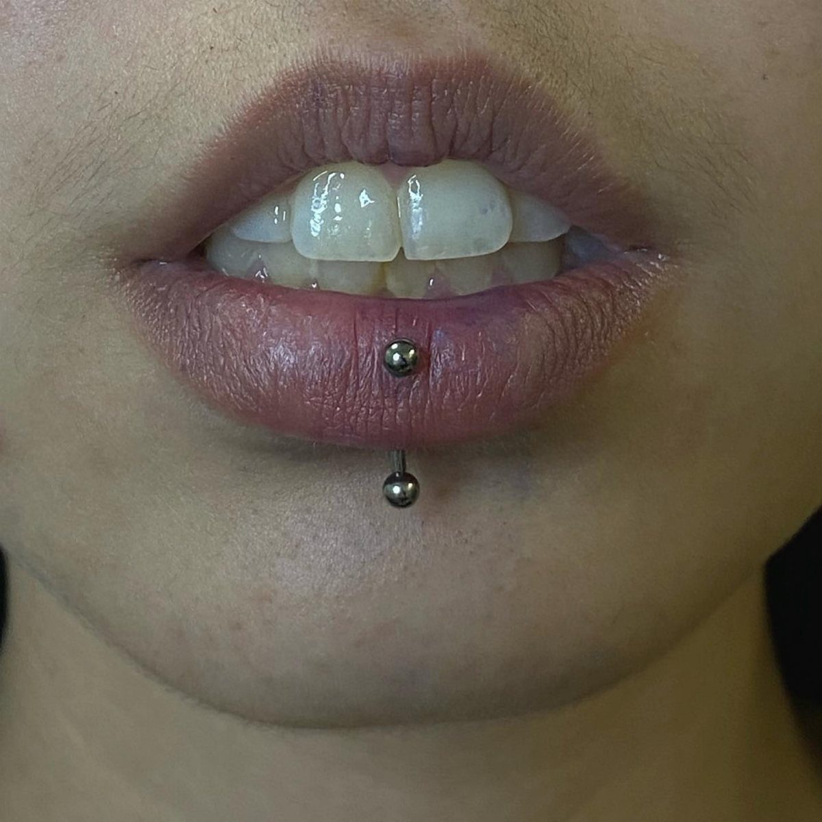 Silver barbell lip piercing centered on a person's lower lip and chin.