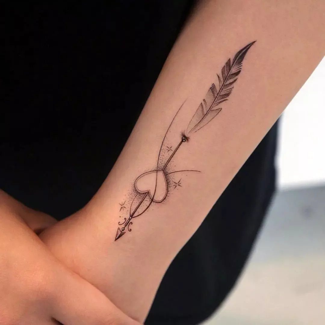 Arrow tattoo with a heart and stars on a person's inner forearm.