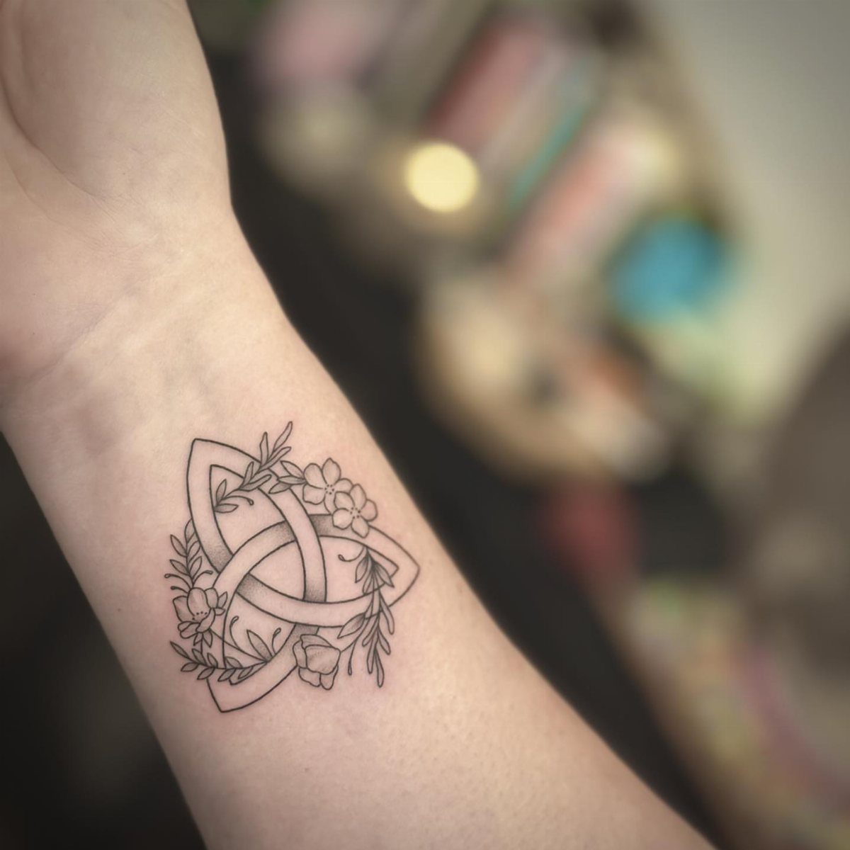 Celtic knot tattoo with floral accents on a person's inner wrist