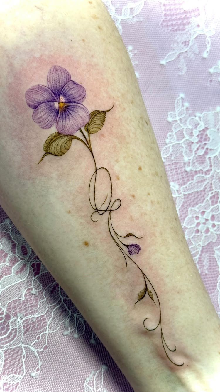 Purple flower tattoo with a swirling stem on a person's fair arm.