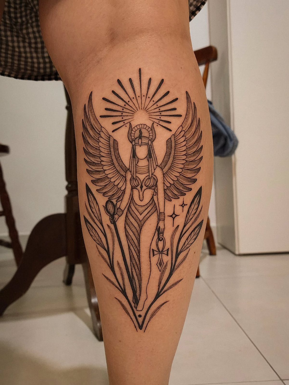 Winged goddess tattoo with an ankh and staff on a person's lower leg