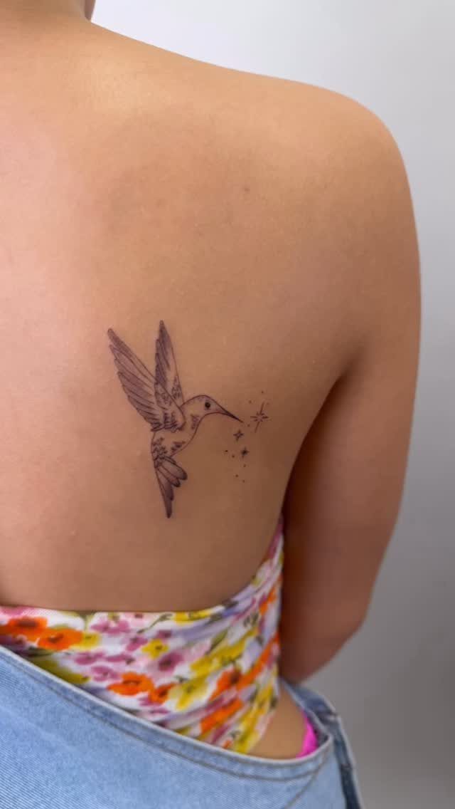 Hummingbird tattoo with small stars on a woman's lower back.