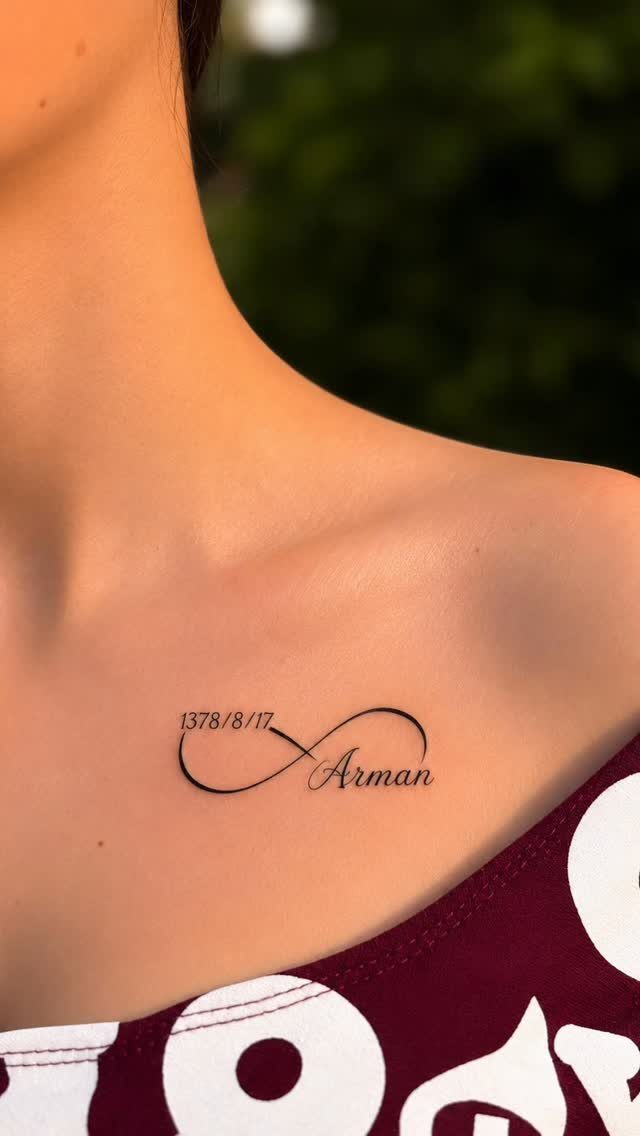 Infinity symbol tattoo on a woman's collarbone with a date and the name Arman.
