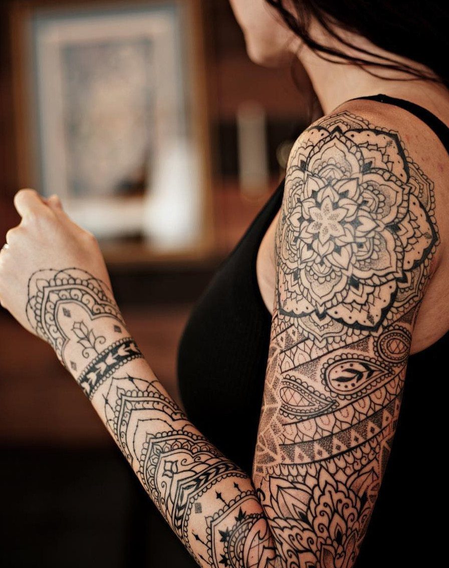 Detailed black ink mandala tattoo on a woman's shoulder and upper arm.