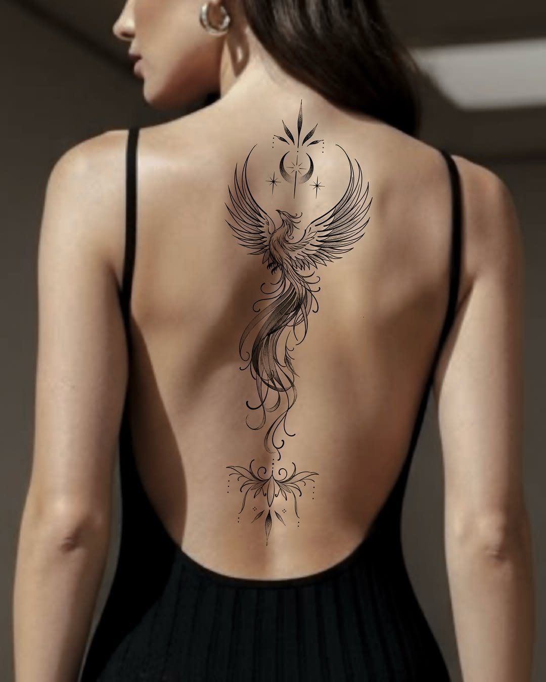 Phoenix tattoo with a crescent moon on a woman's back in a black dress