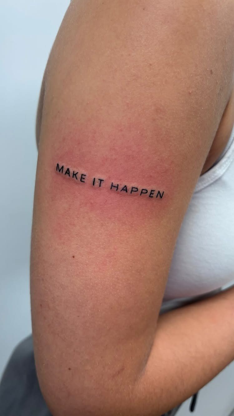 Black ink tattoo on an arm reading MAKE IT HAPPEN in uppercase letters.