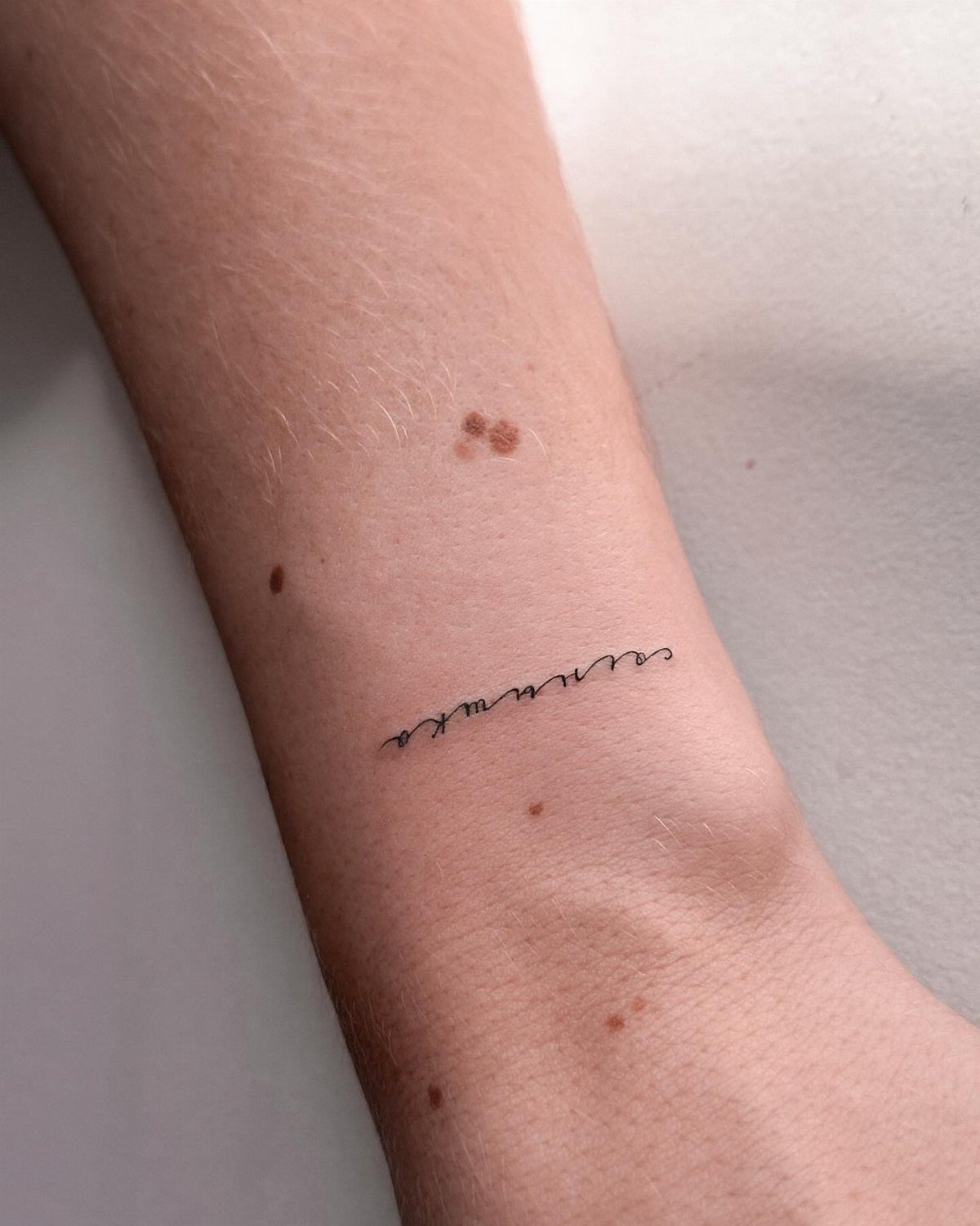 Cursive single word tattoo in black ink on a person's inner forearm.
